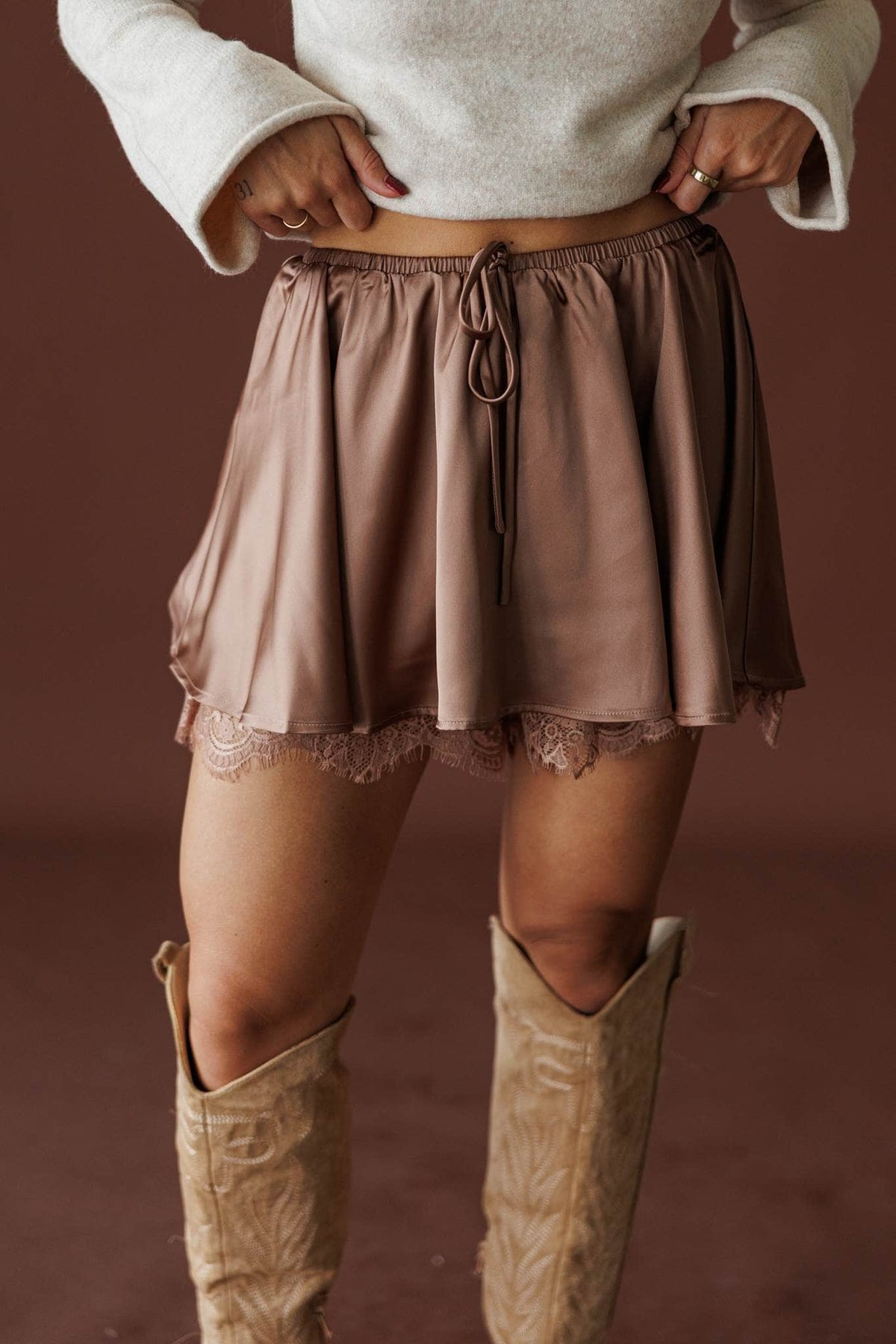 Satin And Lace Skort in bronze, front view of the lace-trimmed hem with tall boots