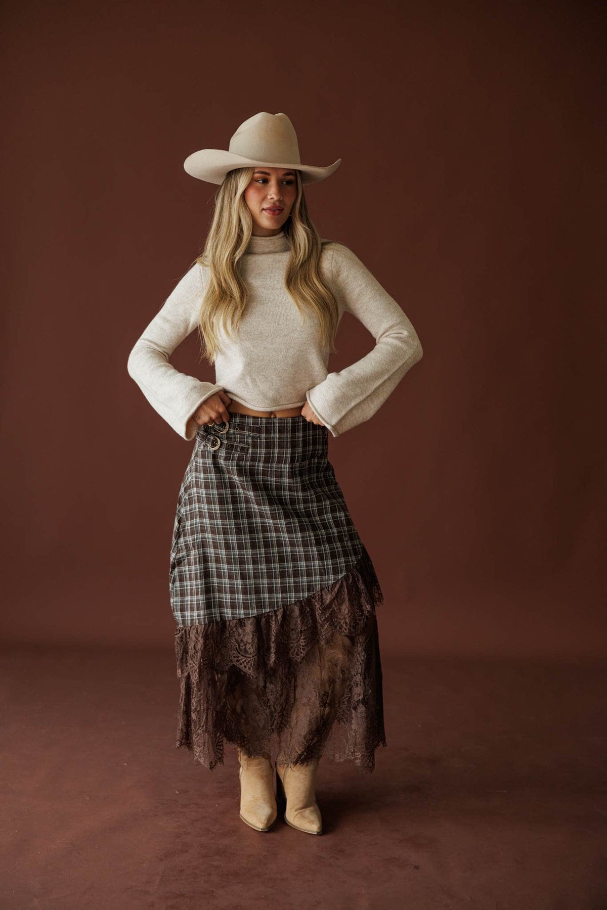 Lost In Wyoming Plaid Skirt in brown, full-length view with a cream sweater and cowboy hat