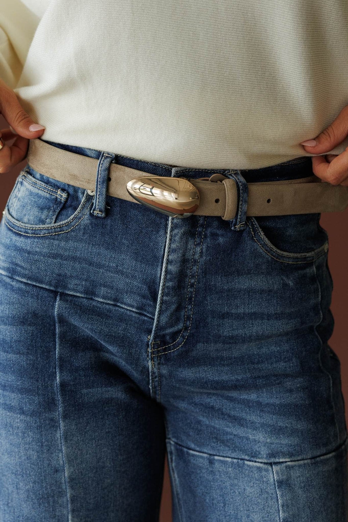 Boston Belt, in dune suede, close front view of the oval buckle over denim