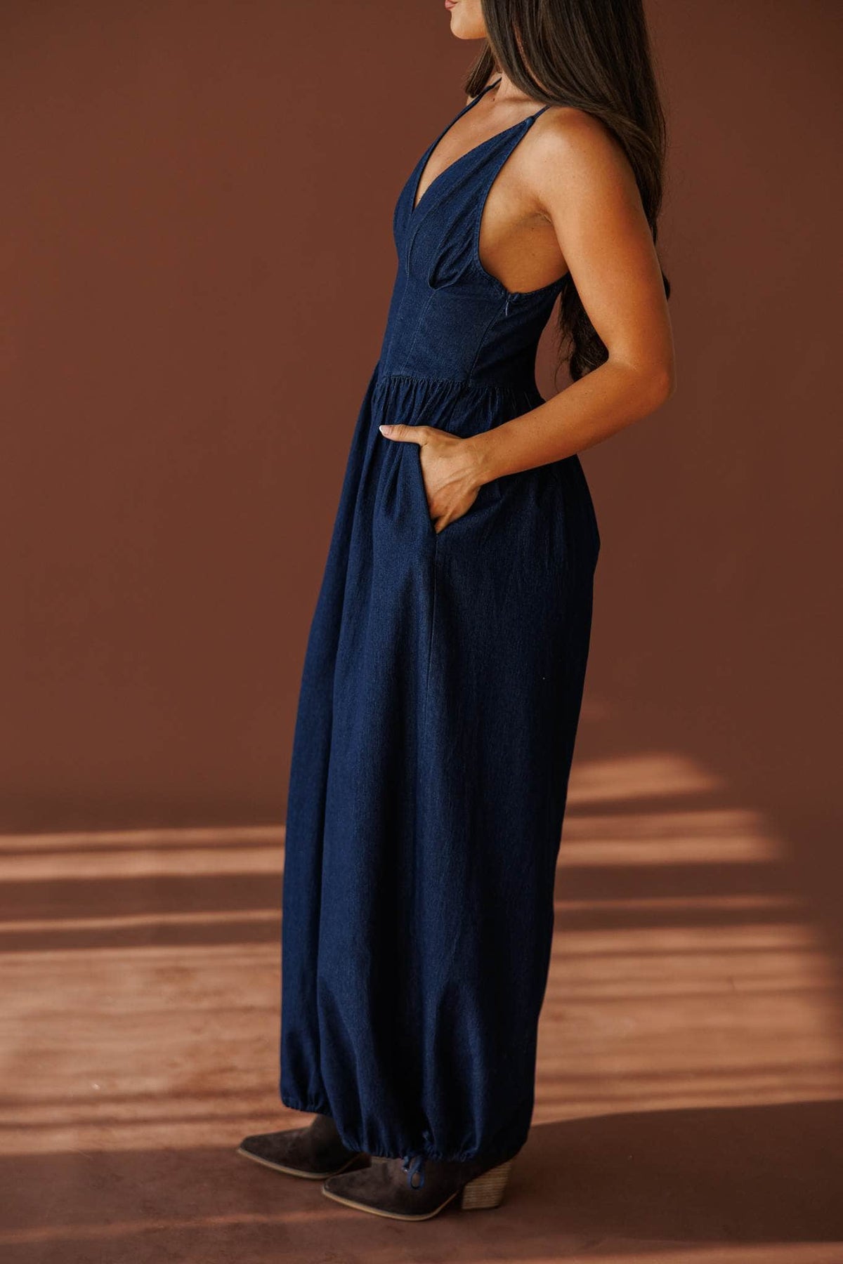 Miles From Home Jumpsuit in dark denim, side view with a hand in the pocket