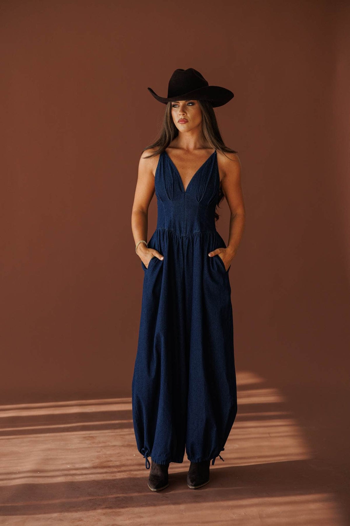 Miles From Home Jumpsuit in dark denim, full-length view with a black hat